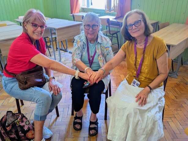 3 women sitting in a semi-circle with arms reaching out to touch in center