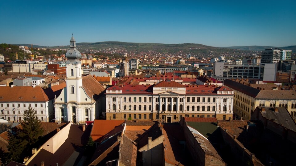 Janos Zsigmond Unitarian High School - large white buildings with red roofs against a backdrop of city and hills