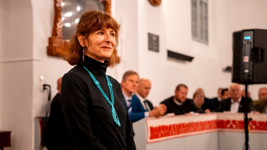 woman with medium-length brown hair and slight smile, wearing black turtleneck and long turquoise necklace with pendant