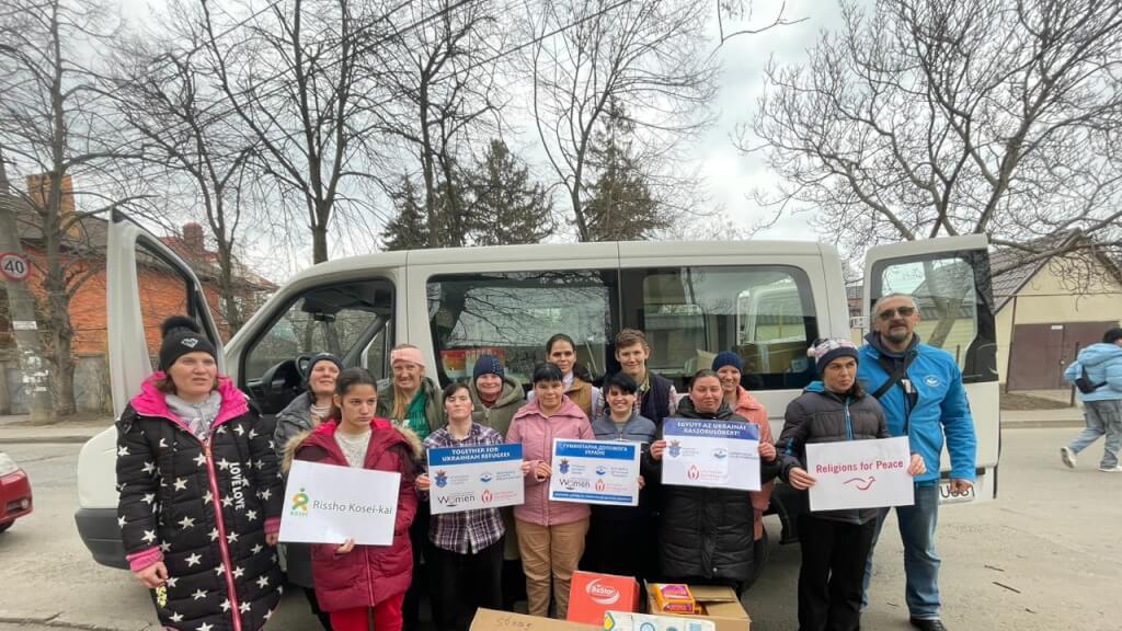 8th Aid Shipment to Southern Ukraine - several people in winter coats standing next to a delivery van holding signs