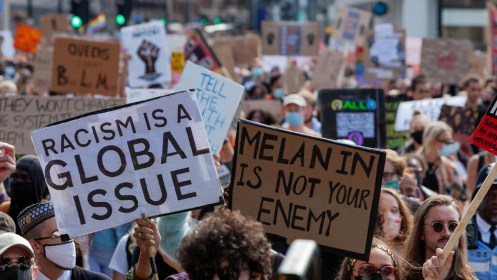 crowd of people with signs protesting racism "Racism is a global issue"