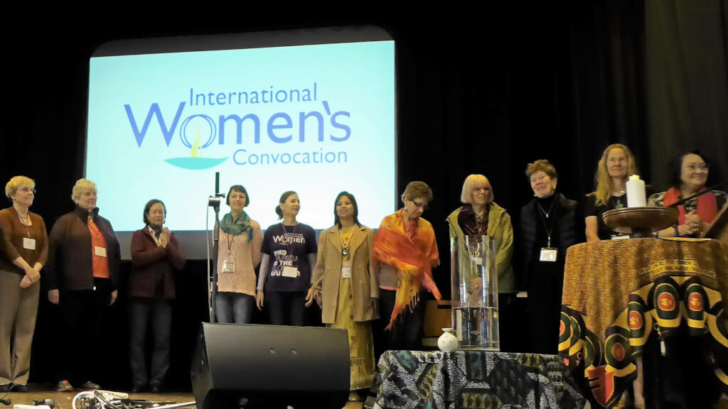 ICUUW team at Third Convo - 11 women on stage with ICUUW logo on screen behind them