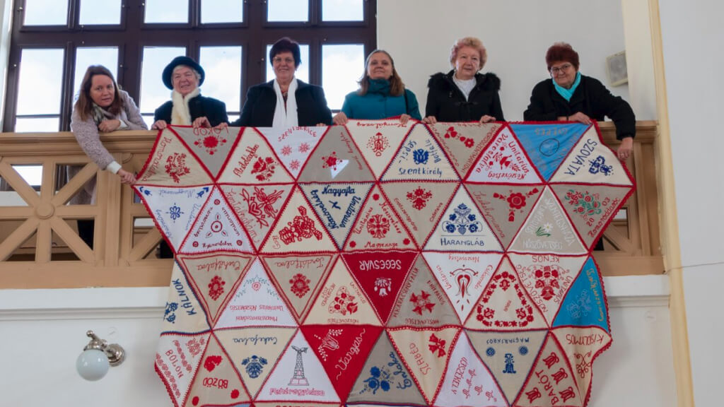 handmade tablecloth handing over railing with 6 women standing above it