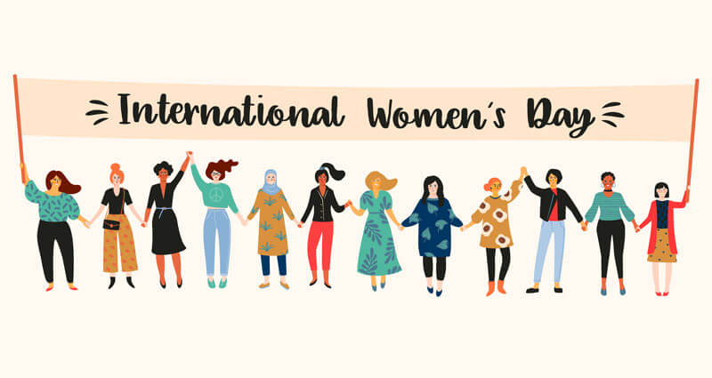 cartoon of women in colorful dress holding up a banner that reads International Women's Day